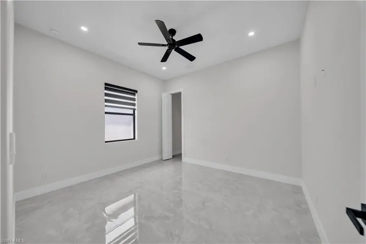 Spacious interior featuring reflective tile flooring, a modern black ceiling fan, and recessed lighting