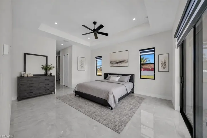 Spacious room featuring large format polished tile flooring, a tray ceiling with recessed lighting, and a ceiling fan
