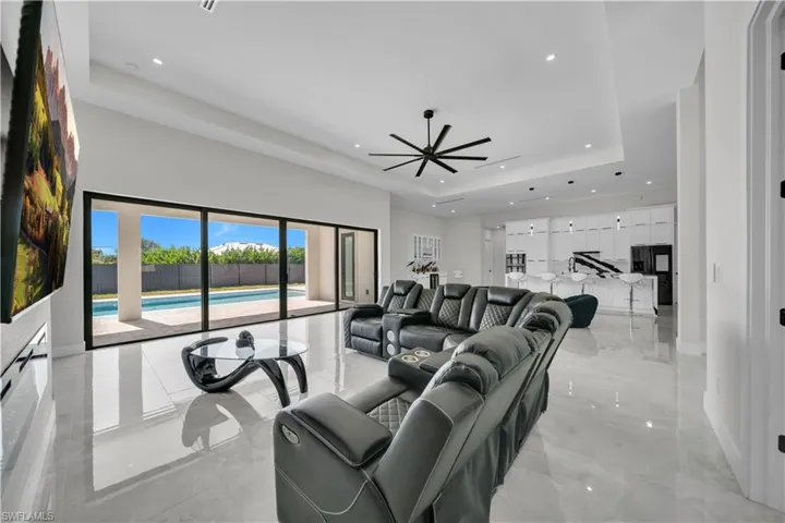 Spacious living area featuring large format tile flooring, a modern black ceiling fan, recessed lighting, and a tray ceiling