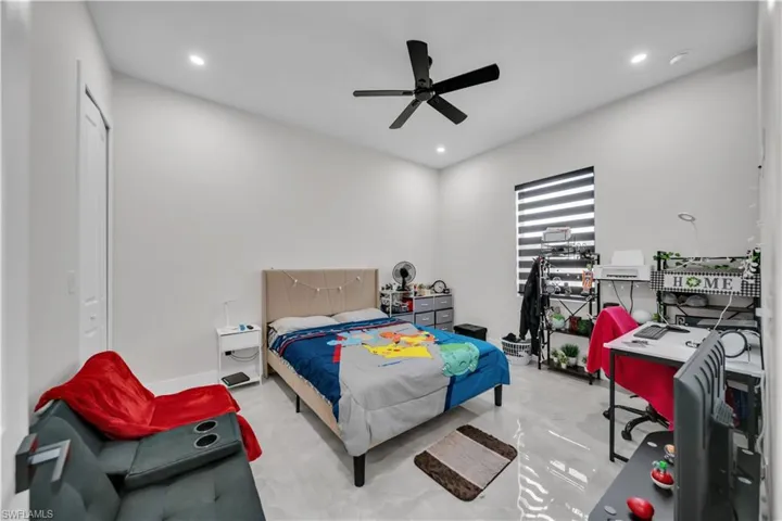 Spacious room featuring light gray flooring, high ceilings with recessed lighting, and a modern black ceiling fan