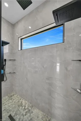 Walk-in shower featuring light grey wall tiling, an elongated window, a black rainfall showerhead, and a hexagonal mosaic tile floor