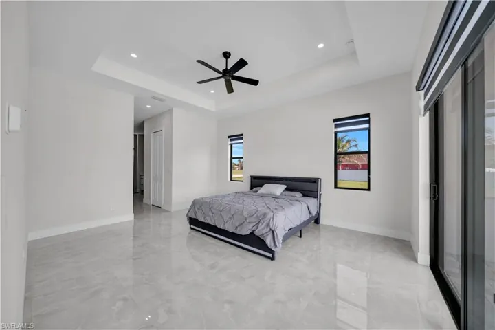 Spacious room featuring large format tile flooring, a tray ceiling with recessed lighting, an overhead ceiling fan, and sliding glass doors