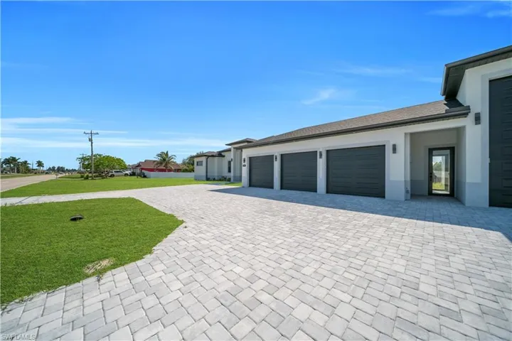 Exterior featuring a paver driveway, multiple garage doors, a covered entry, exterior wall sconces, and a partial view of a landscaped lot