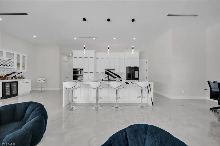 Modern kitchen featuring white cabinetry, a large center island with a waterfall countertop, integrated appliances, and pendant lighting