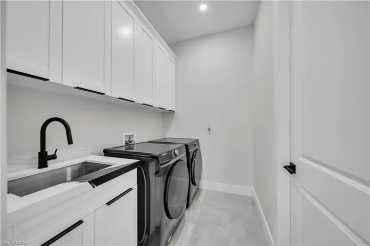 Laundry room featuring white cabinetry with dark hardware, a utility sink with a matte black faucet, and light-toned flooring