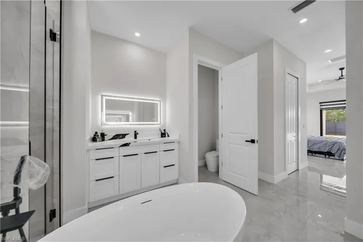 Spacious bathroom featuring a freestanding tub, double vanity with an illuminated mirror, glass-enclosed shower, and large format tile flooring