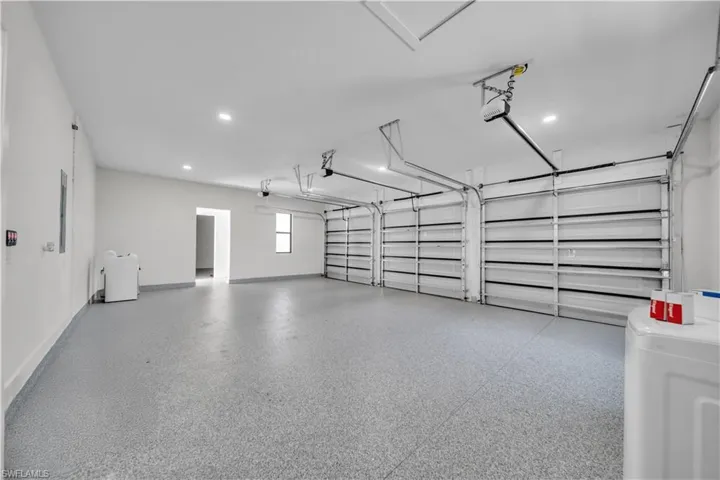 Spacious three-car garage featuring a speckled epoxy floor finish, overhead garage door openers, recessed lighting, and a window for natural light