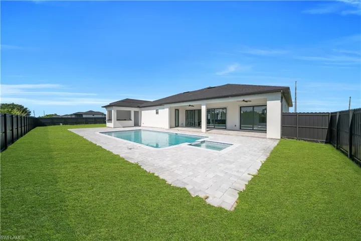 Expansive backyard featuring a rectangular pool with an integrated spa, a paved patio area, and a covered outdoor living space with recessed lighting and ceiling fans