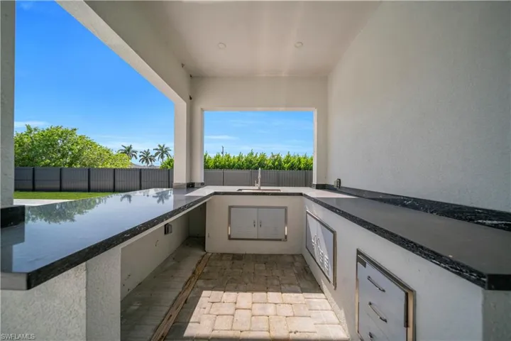 Outdoor kitchen featuring stone-finish countertops, stainless steel cabinet doors, a built-in sink, and paver flooring