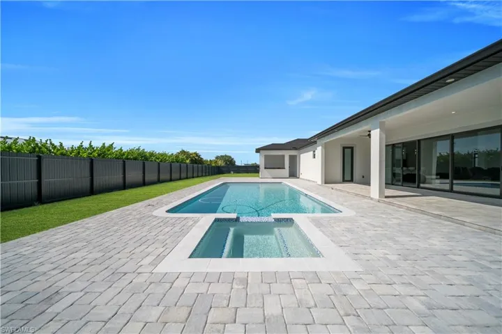Expansive paver patio featuring a rectangular swimming pool with integrated spa and a perimeter of green lawn