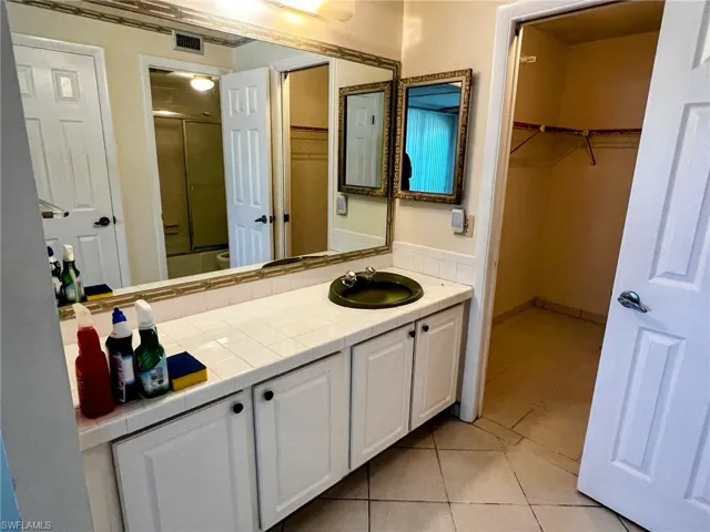 Bathroom with a shower with shower door, tile patterned floors, vanity, and a spacious closet