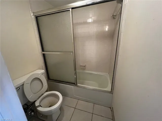 Bathroom with tile patterned flooring, shower / bath combination with glass door, and toilet