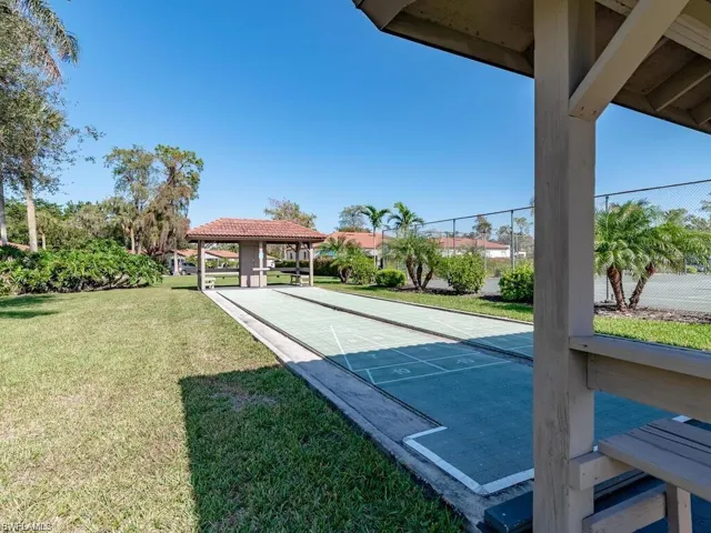 View of home's community featuring shuffleboard, fence, and a lawn