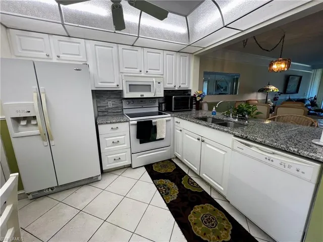 Kitchen with dark stone countertops, white appliances, light tile patterned floors, white cabinetry, and a sink