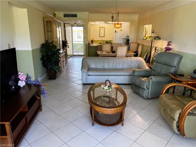 Living room with light tile patterned floors, visible vents, a textured ceiling, and ornamental molding