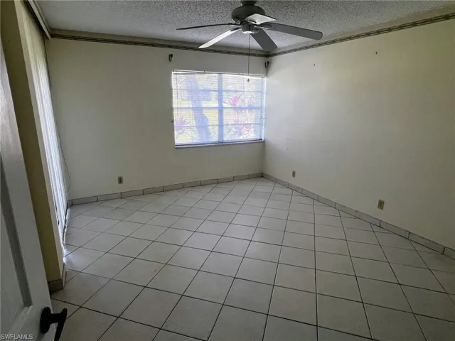 Empty room featuring ceiling fan, light tile patterned flooring, and a textured ceiling