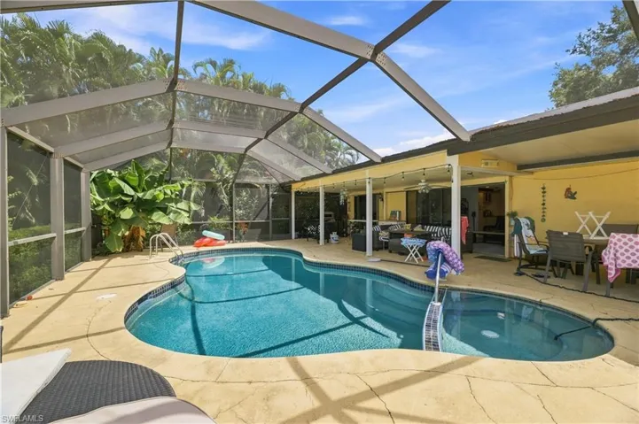 Screened-in swimming pool with a freeform design, concrete surround, and a covered patio area featuring an exterior ceiling fan