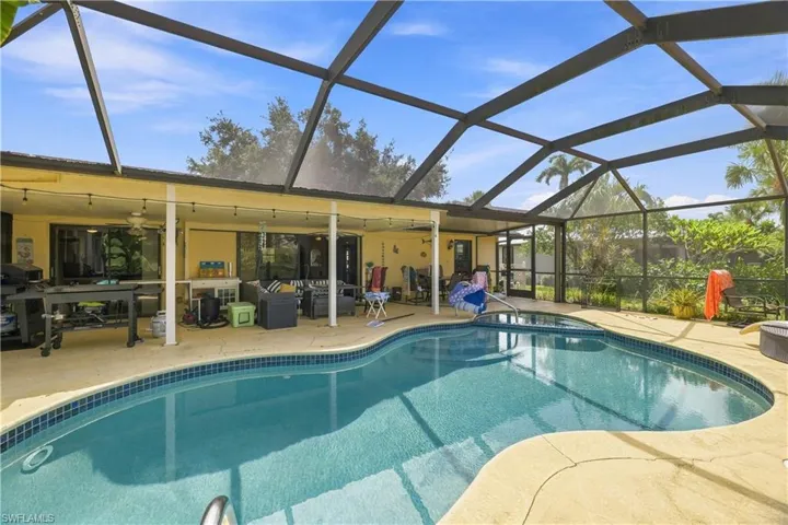 Screened-in pool deck featuring a freeform pool with tile trim, a covered patio, and multiple sliding glass doors