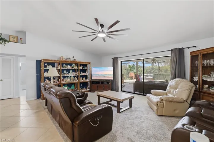 Vaulted ceiling with a contemporary ceiling fan, tile flooring, built-in shelving, and sliding glass doors opening to the screened outdoor area