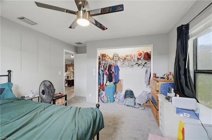 Carpeted flooring, ceiling fan with integrated lighting, open closet with hanging rod, and a window with dark curtains