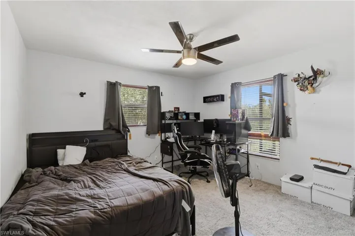 Ceiling fan with integrated lighting, two windows with horizontal blinds, neutral wall paint, and carpeted flooring