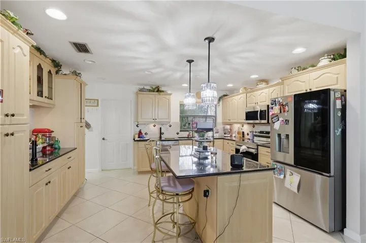 Kitchen featuring light-toned cabinetry, a central island with a dark countertop, recessed lighting, and tile flooring
