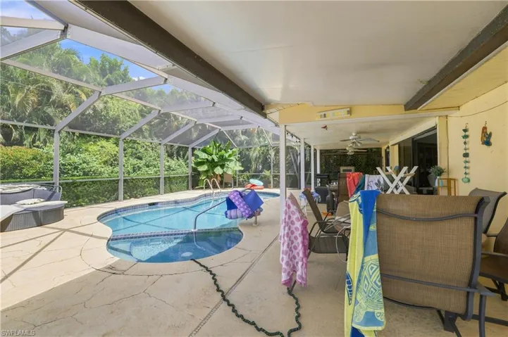 Screened-in pool enclosure featuring a freeform pool, concrete deck, and covered patio area with ceiling fans