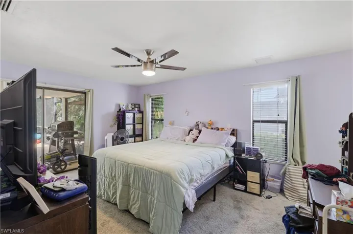 Sliding glass door access to an outdoor screened area, ceiling fan with integrated lighting, window with blinds, and carpeting