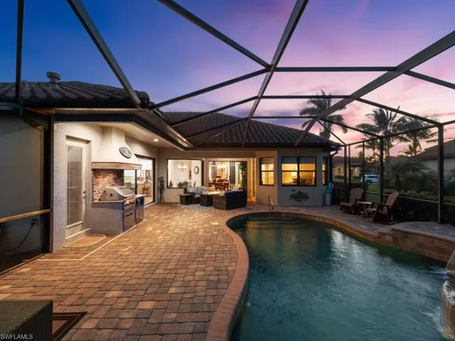 Pool at dusk featuring a patio, an outdoor hangout area, an outdoor pool, exterior kitchen, and glass enclosure