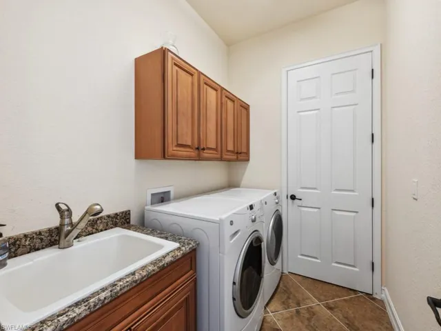 Washroom with a sink, baseboards, separate washer and dryer, cabinet space, and dark tile patterned flooring