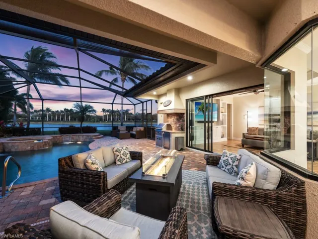 Patio terrace at dusk with an outdoor living space with a fire pit, a water view, a lanai, an outdoor kitchen, and a pool with connected hot tub