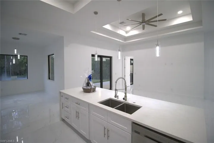 Kitchen with a raised ceiling, sink, pendant lighting, and white cabinets