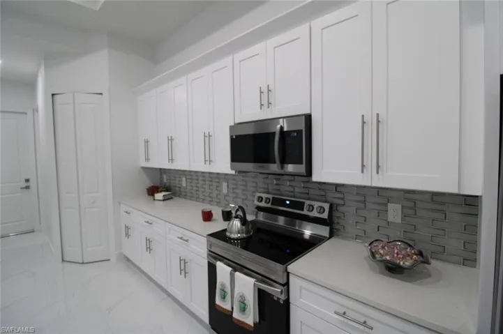 Kitchen with tasteful backsplash, white cabinets, and appliances with stainless steel finishes