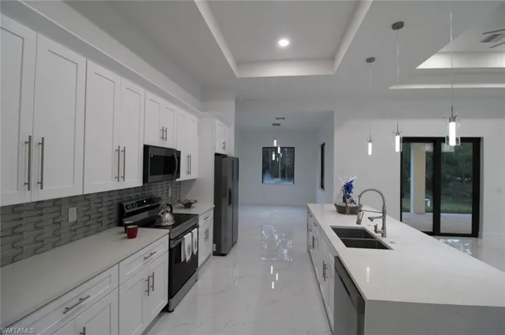 Kitchen featuring pendant lighting, sink, stainless steel appliances, white cabinets, and a center island with sink