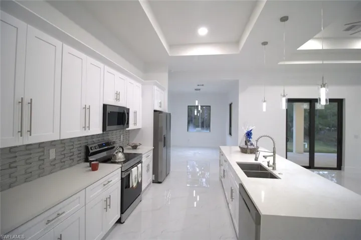 Kitchen featuring sink, stainless steel appliances, white cabinets, decorative light fixtures, and a raised ceiling
