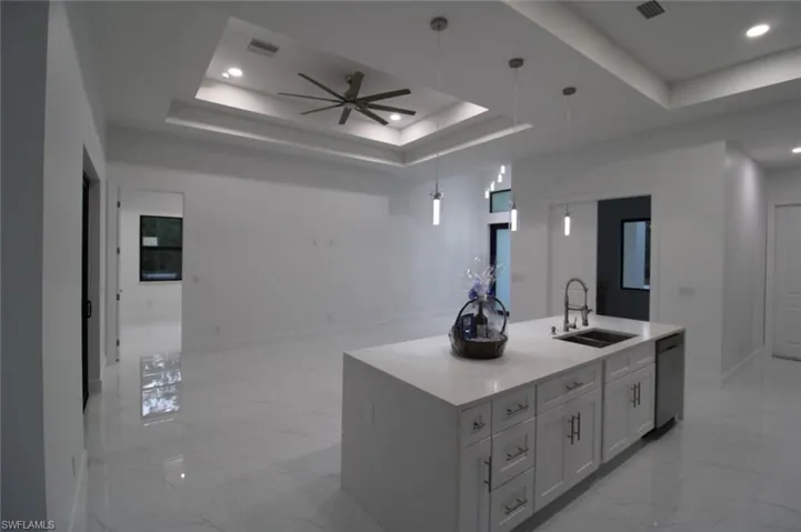 Kitchen featuring a raised ceiling, stainless steel dishwasher, sink, and a center island with sink