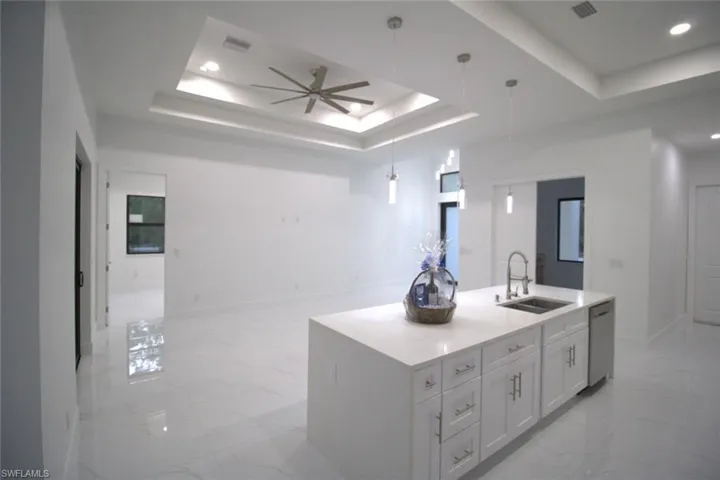 Kitchen with white cabinetry, sink, hanging light fixtures, a kitchen island with sink, and a tray ceiling