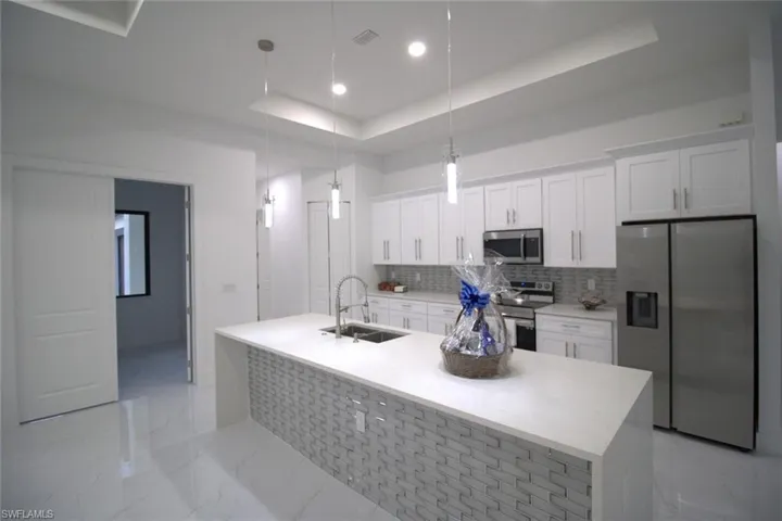 Kitchen with pendant lighting, sink, appliances with stainless steel finishes, white cabinetry, and a tray ceiling