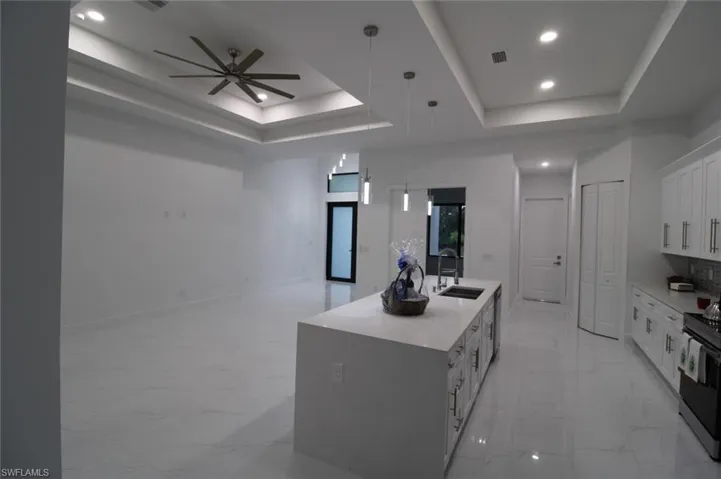 Kitchen featuring white cabinetry, sink, hanging light fixtures, a kitchen island with sink, and a raised ceiling