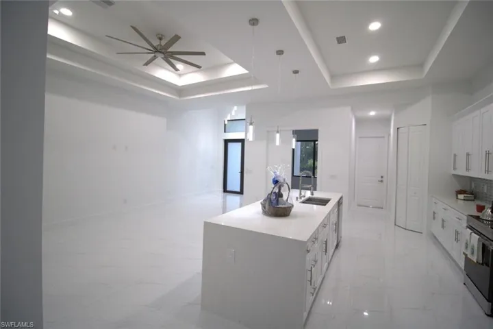 Kitchen with an island with sink, sink, white cabinets, and a tray ceiling
