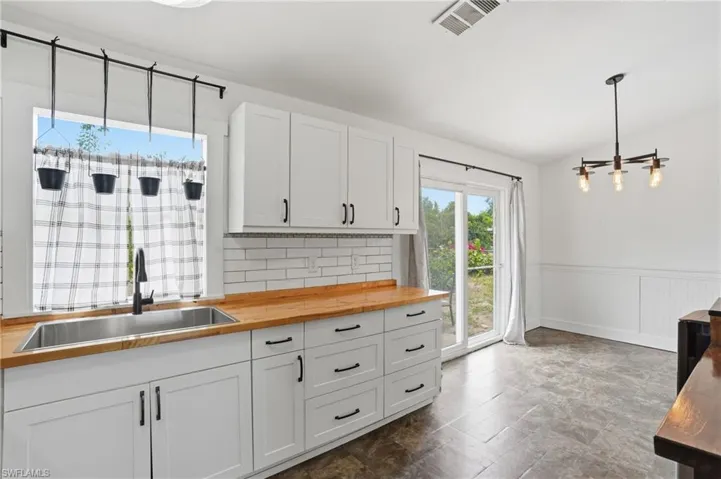 Kitchen featuring white shaker cabinetry, butcher block countertops, a stainless steel sink with a matte black faucet, and a subway tile backsplash