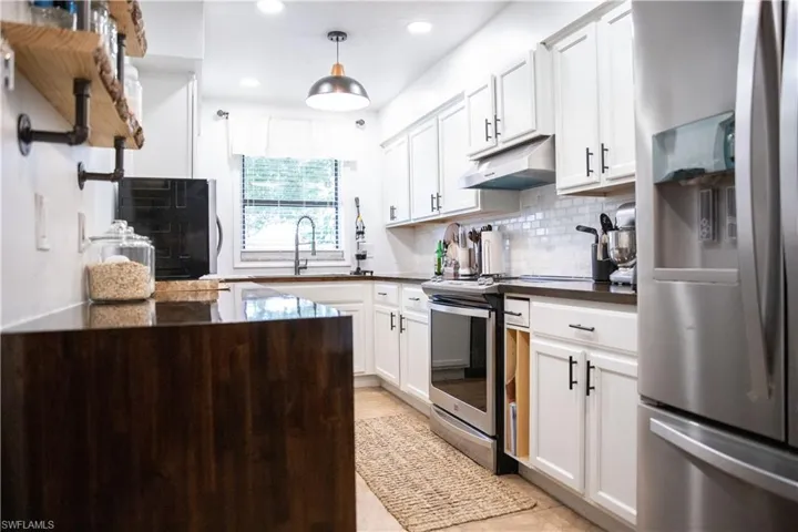 Kitchen with appliances with stainless steel finishes, backsplash, white cabinets, under cabinet range hood, and recessed lighting