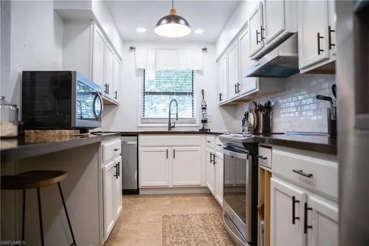 Kitchen featuring dark countertops, stainless steel appliances, under cabinet range hood, recessed lighting, and white cabinets