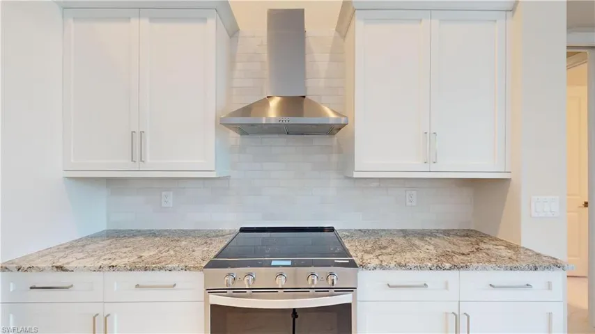 Kitchen with white cabinets, stainless steel stove, and wall chimney range hood