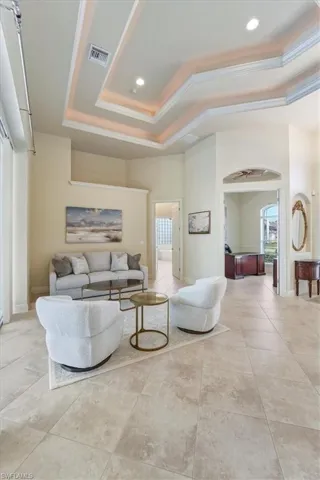 Living area featuring a raised ceiling, crown molding, arched walkways, light tile patterned floors, and recessed lighting