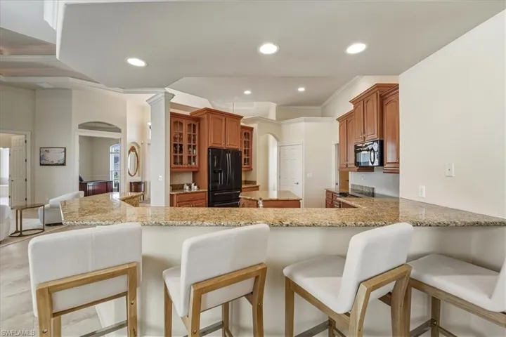 Kitchen featuring arched walkways, a breakfast bar, black appliances, light stone countertops, and brown cabinetry