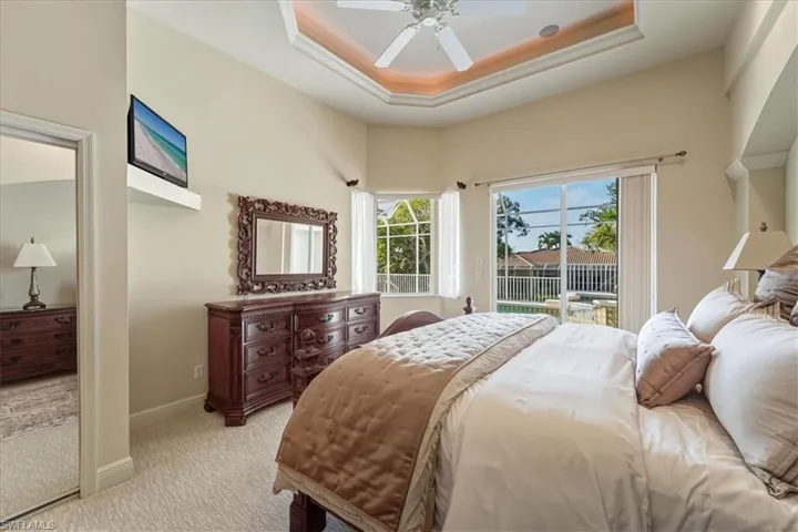 Bedroom with access to exterior, a raised ceiling, carpet floors, and a ceiling fan
