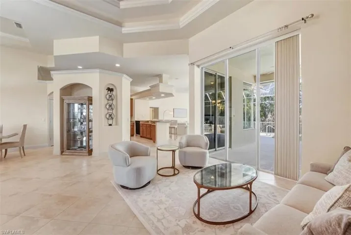 Living area with a raised ceiling, arched walkways, and crown molding