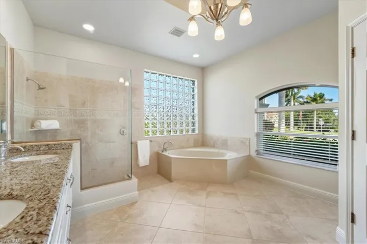 Bathroom with a garden tub, double vanity, a stall shower, light tile patterned floors, and a chandelier