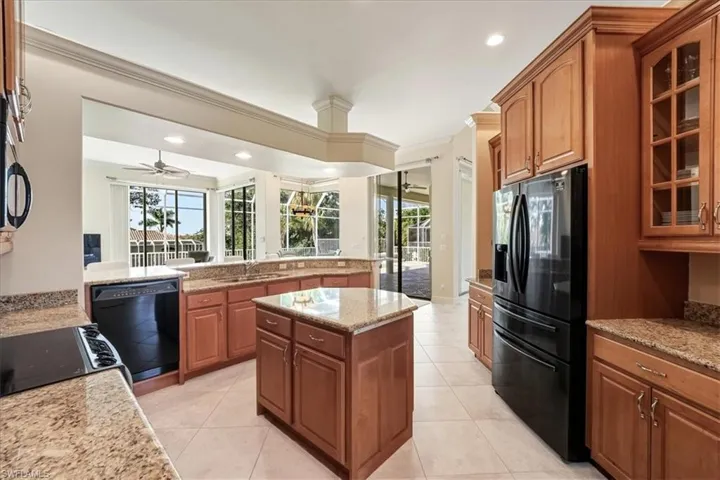 Kitchen featuring black appliances, brown cabinets, light stone counters, glass insert cabinets, and a kitchen island